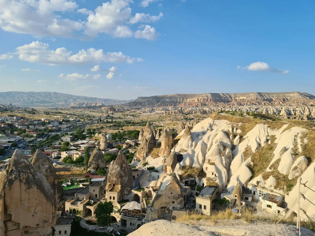 Wide aerial perspective of dozens of colorful hot air balloons filling the sky above the vast, textured fairy chimney landscapes of Cappadocia.