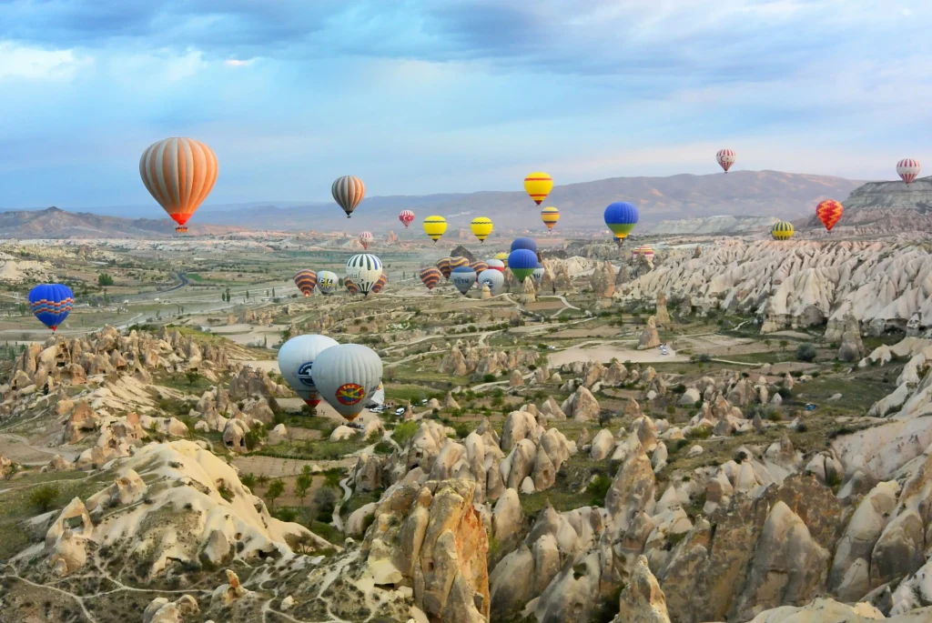 Panoramic view of Göreme town in Cappadocia showing traditional stone buildings and cave houses carved into volcanic tuff formations under a bright blue sky.