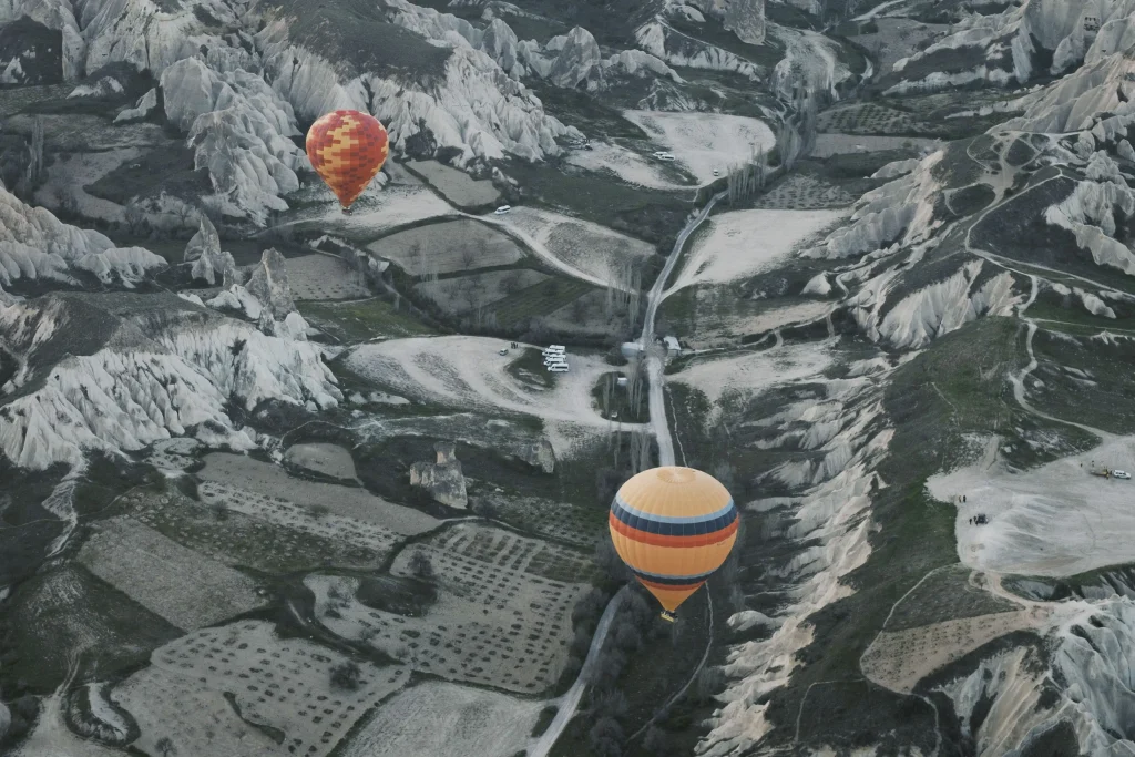 Aerial high angle view of colorful hot air balloons flying over volcanic rock formations and fields in Cappadocia