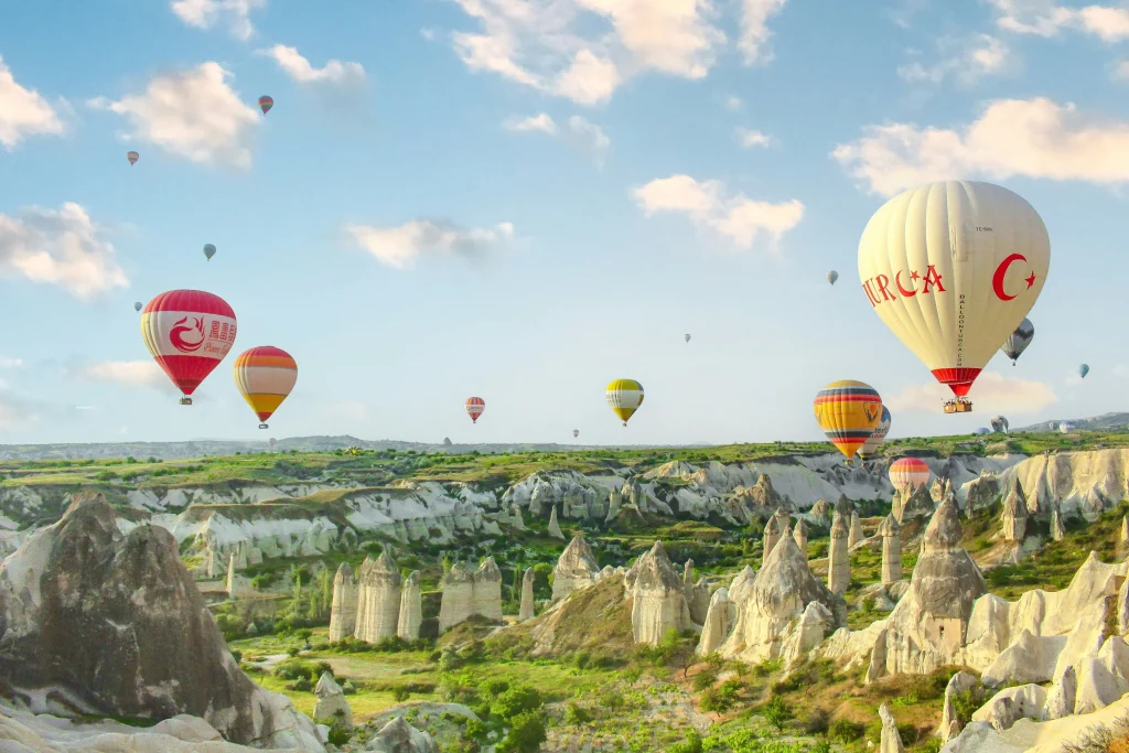 Dozens of vibrant hot air balloons drifting over famous fairy chimneys and green valleys in Cappadocia under a blue sky